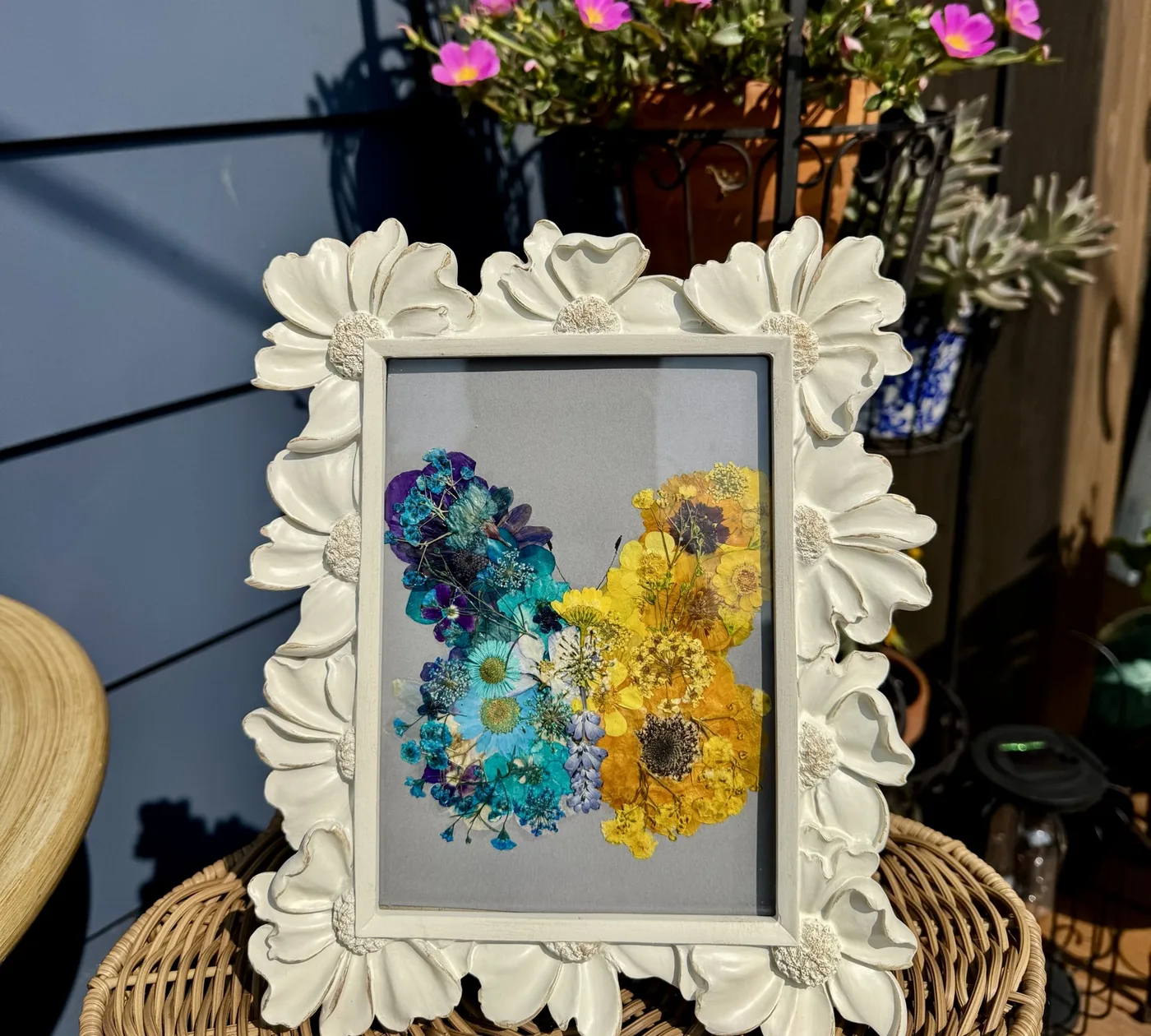 An ornate white frame of blue and yellow pressed flowers echoing the logo