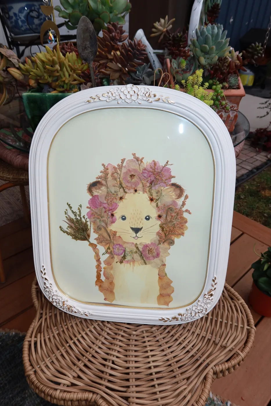 A pressed flower lion with a pink floral mane in an arched white frame