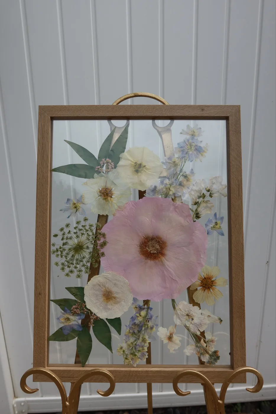 A tall wood frame of pressed flowers centered on a large pink bloom