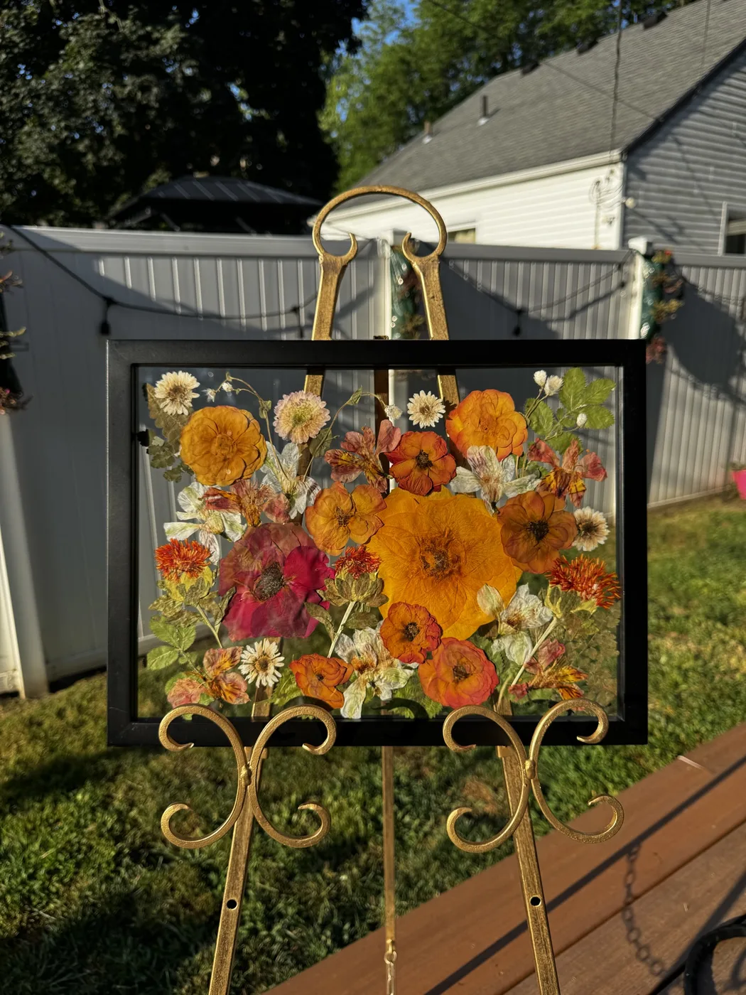 A black frame of pressed orange and red flowers on an easel