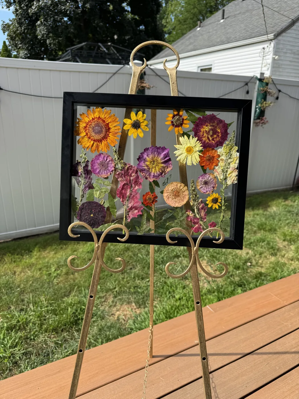 A black frame of pressed sunflowers and wildflowers on an easel